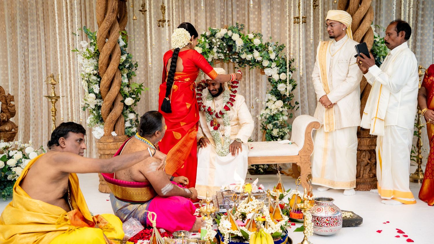 South Indian couple perform traditional garland exchange ritual at Hindu wedding with priests present.