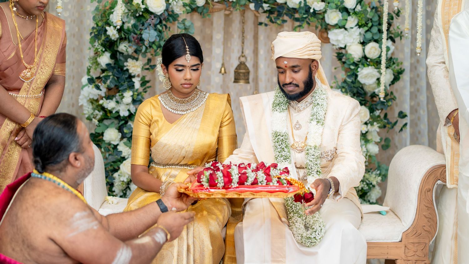 A couple receives a ceremonial tray with flowers during their traditional wedding ceremony with floral decorations.