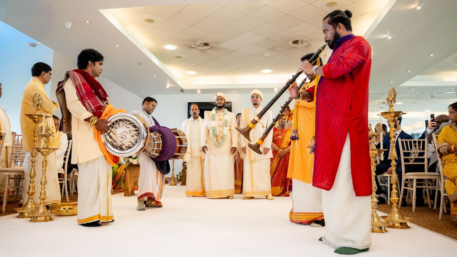 South Indian wedding musicians performing with drums and nadaswaram in a decorated venue.