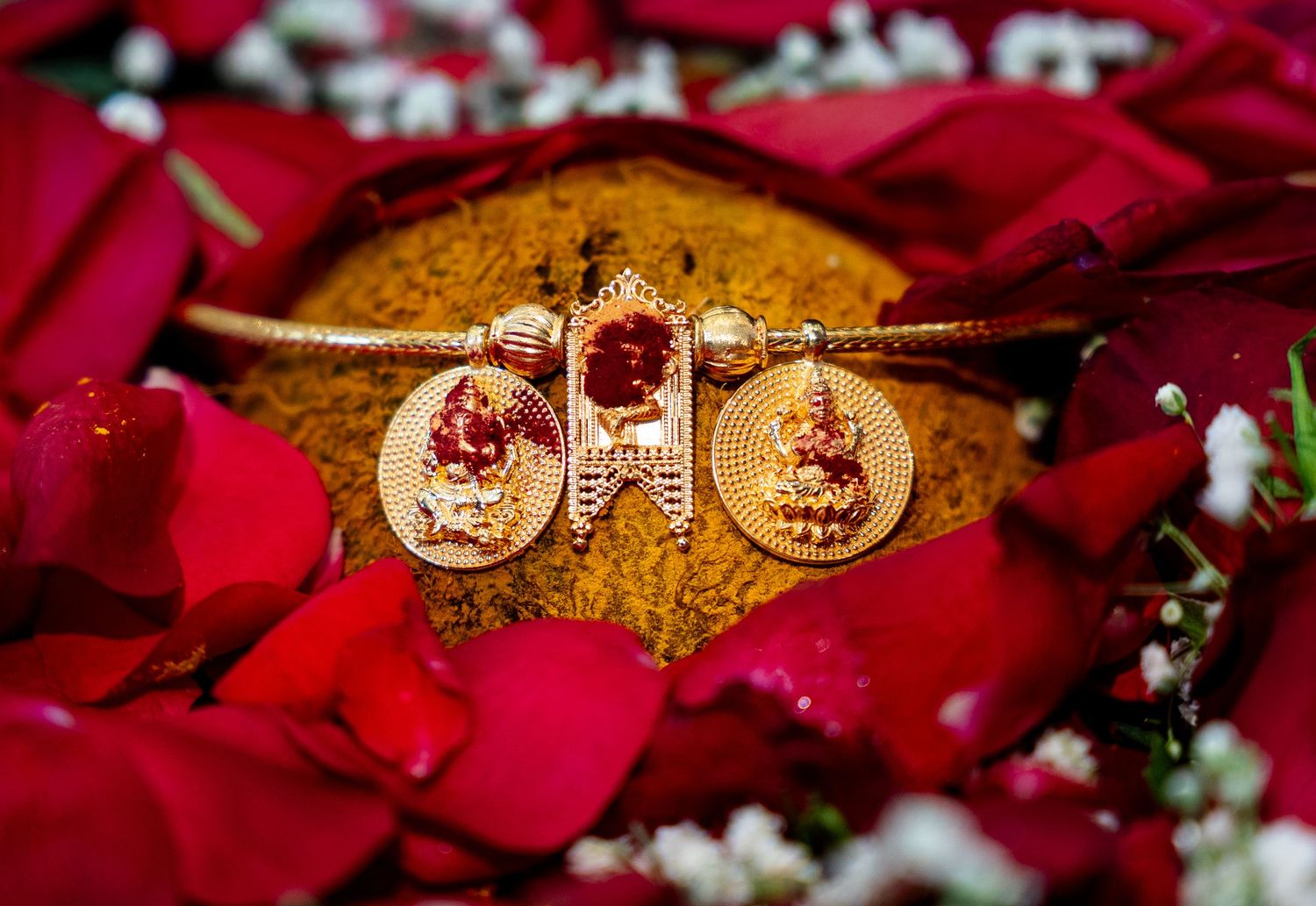 Close-up of gold Hindu wedding bangle featuring Lakshmi deity pendants with red stones on rose petals.