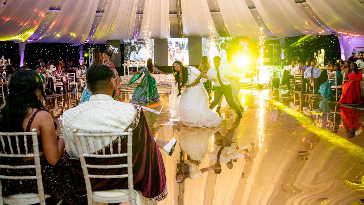 Couple shares first dance at elegant outdoor wedding reception with golden sunset light and guests seated at white chairs.