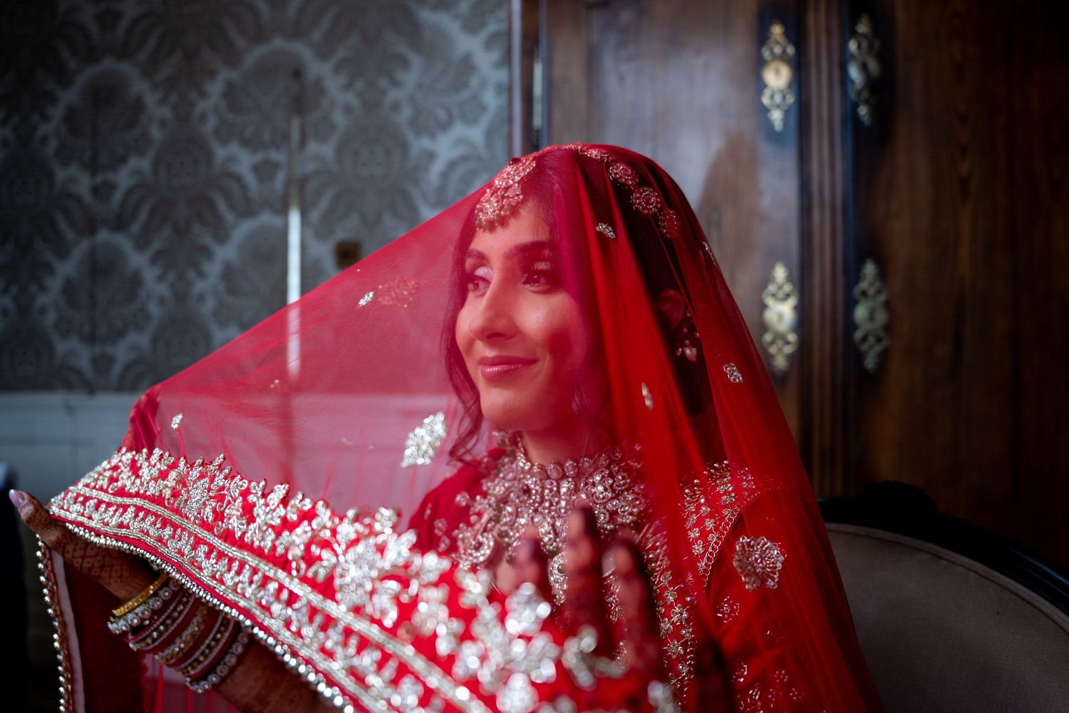 Smiling Indian bride wearing red dupatta veil and elaborate bridal jewelry.