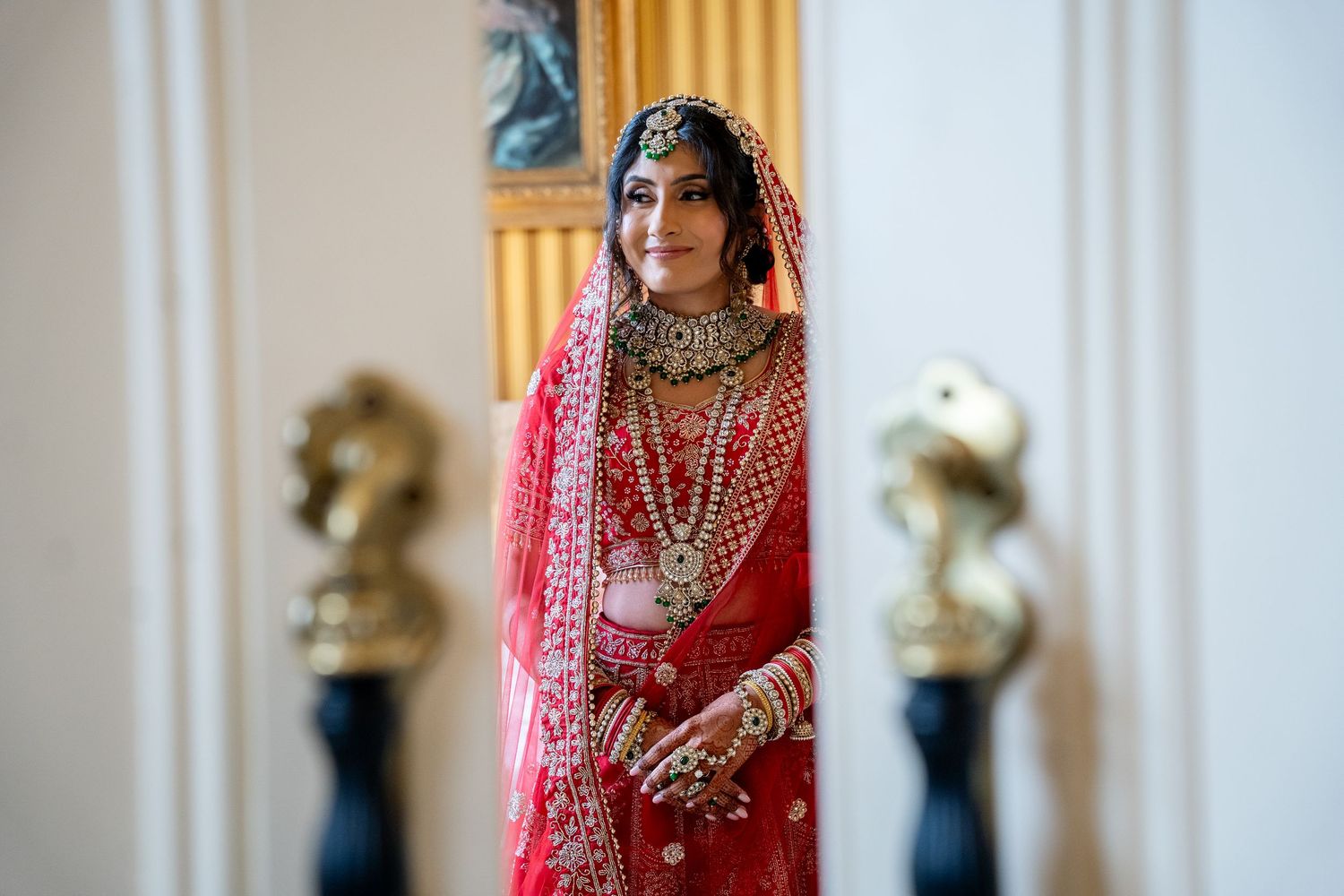 South Asian bride in red lehenga with gold jewelry and maang tikka poses elegantly in traditional bridal attire.