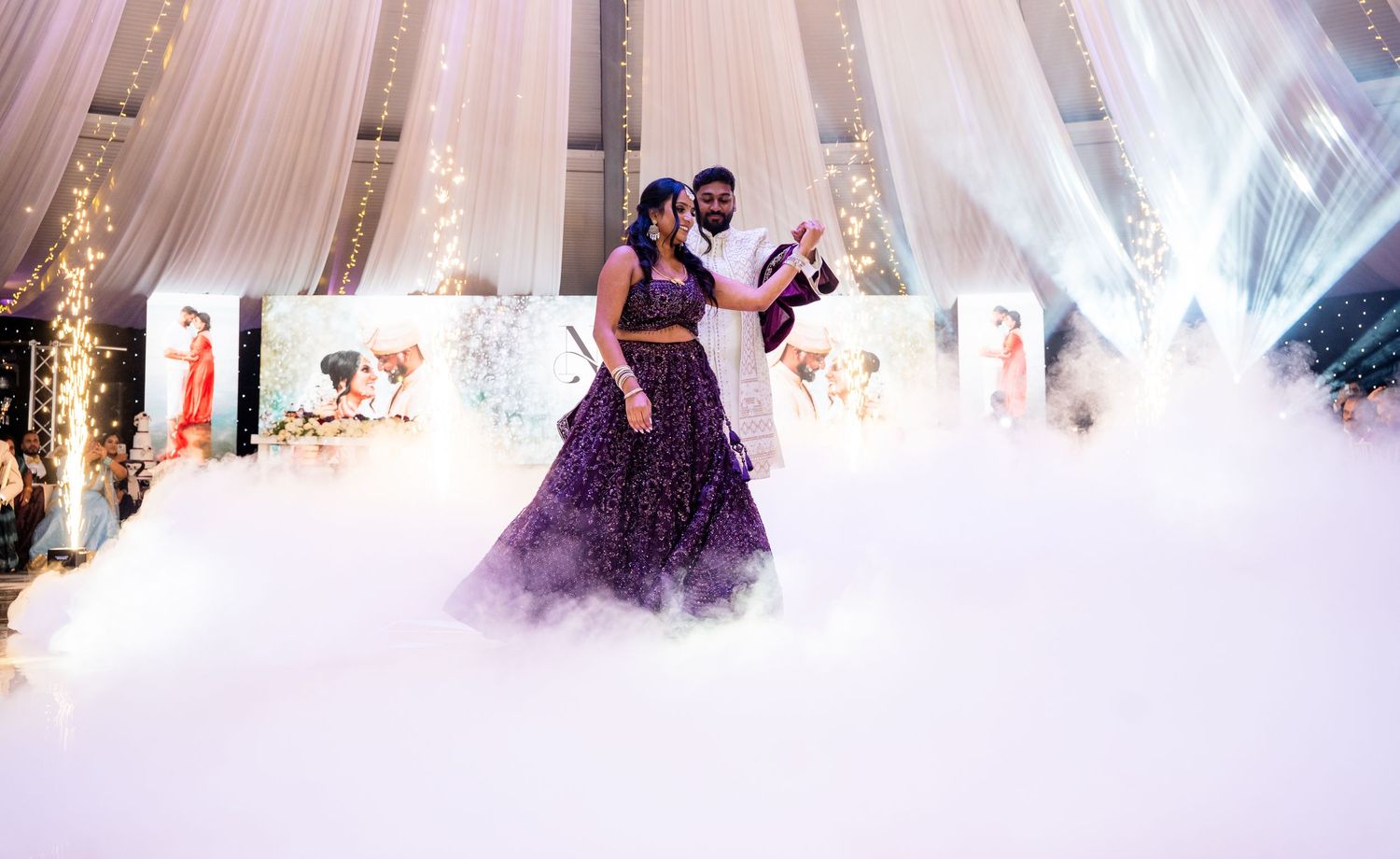 Couple dancing on a foggy dance floor at an Indian wedding reception in a beautifully decorated venue.