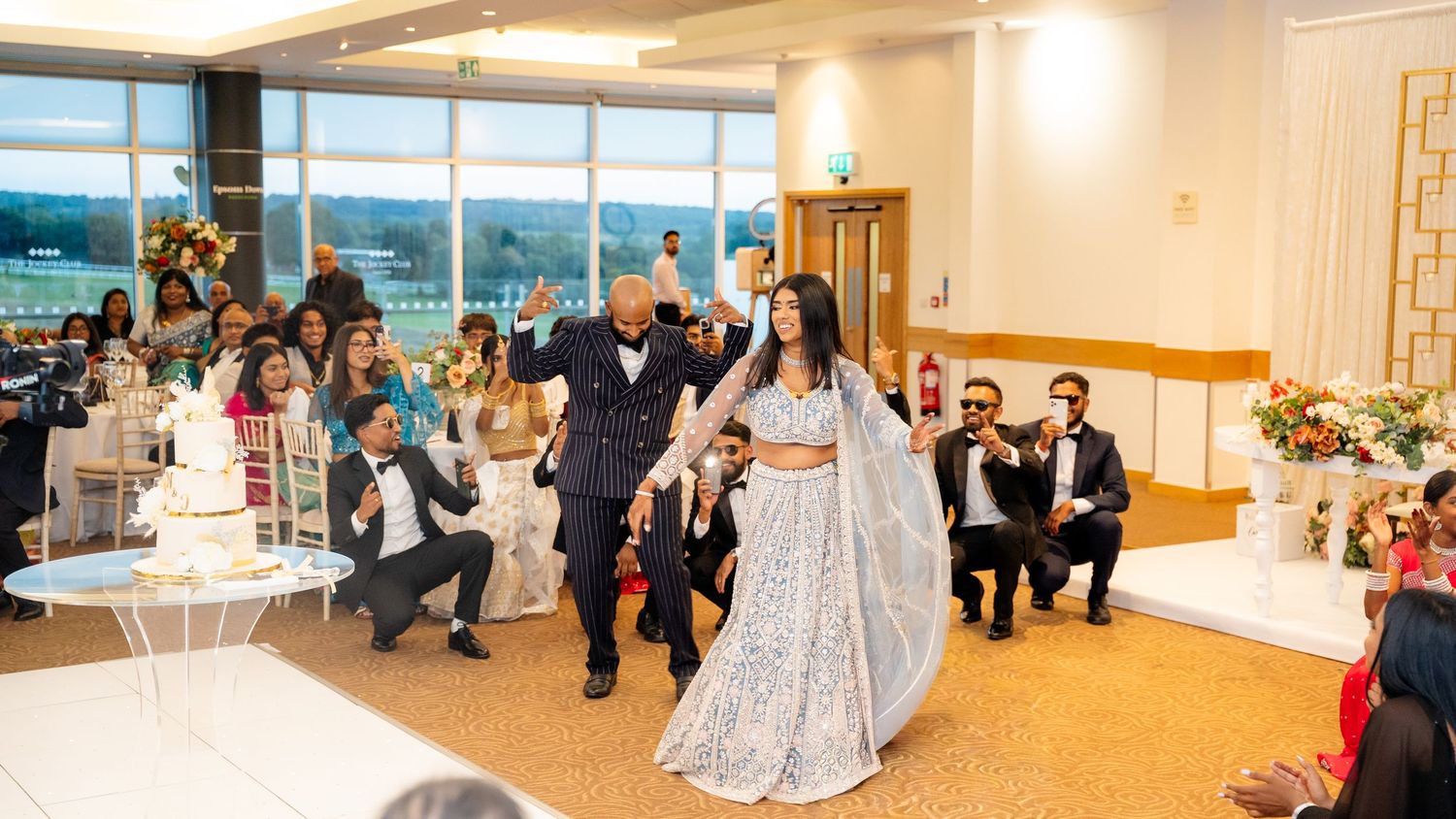 Bride in blue lehenga makes grand entrance with guests cheering at elegant wedding reception.