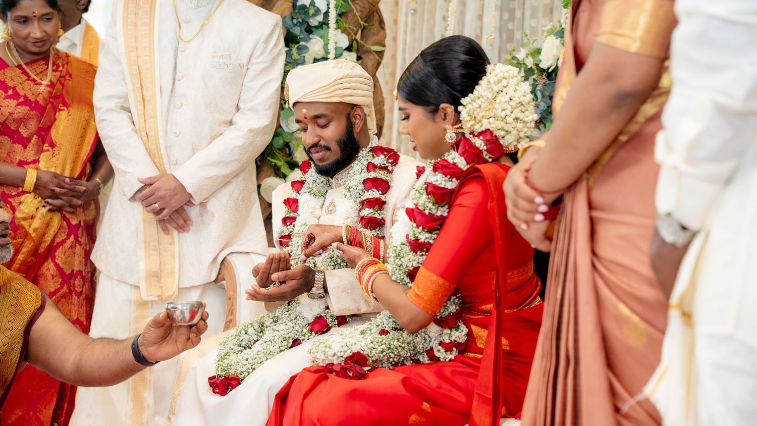 Bride and groom sit together during South Indian wedding rituals while priest performs sacred ceremonies.