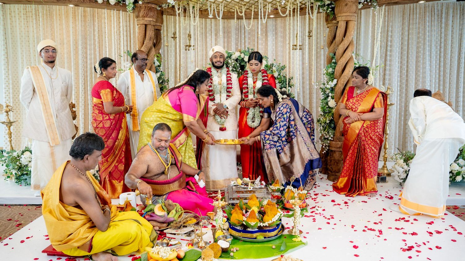 Traditional South Indian Hindu wedding ceremony with priest, family, bride and groom surrounded by rose petals.