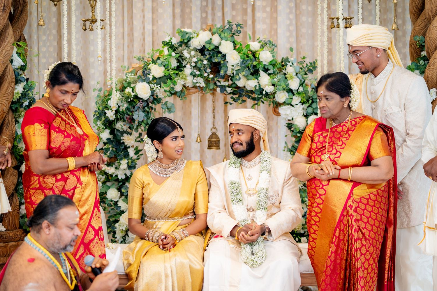 South Indian wedding couple seated at decorated mandap with family members and priest performing traditional rituals.