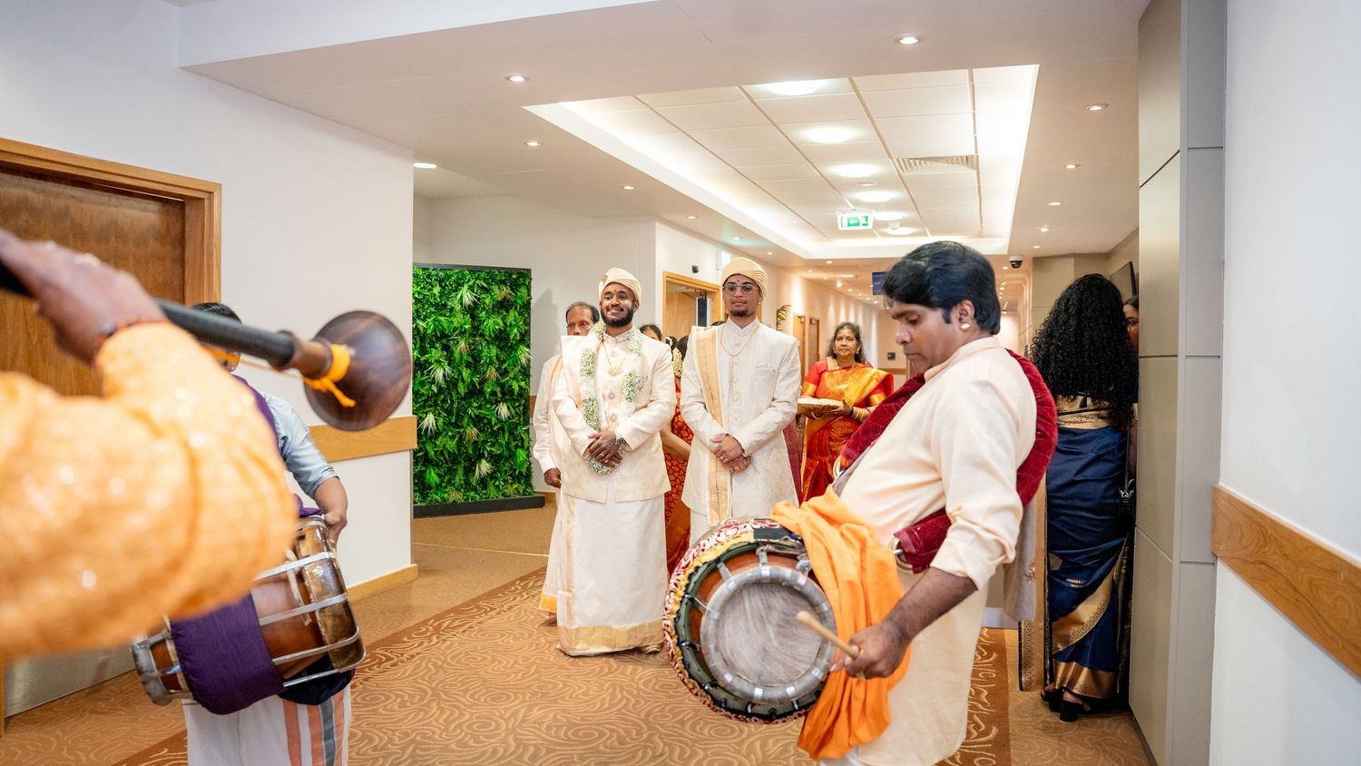 Traditional South Indian wedding ceremony with drummers in orange attire performing in a decorated hallway.