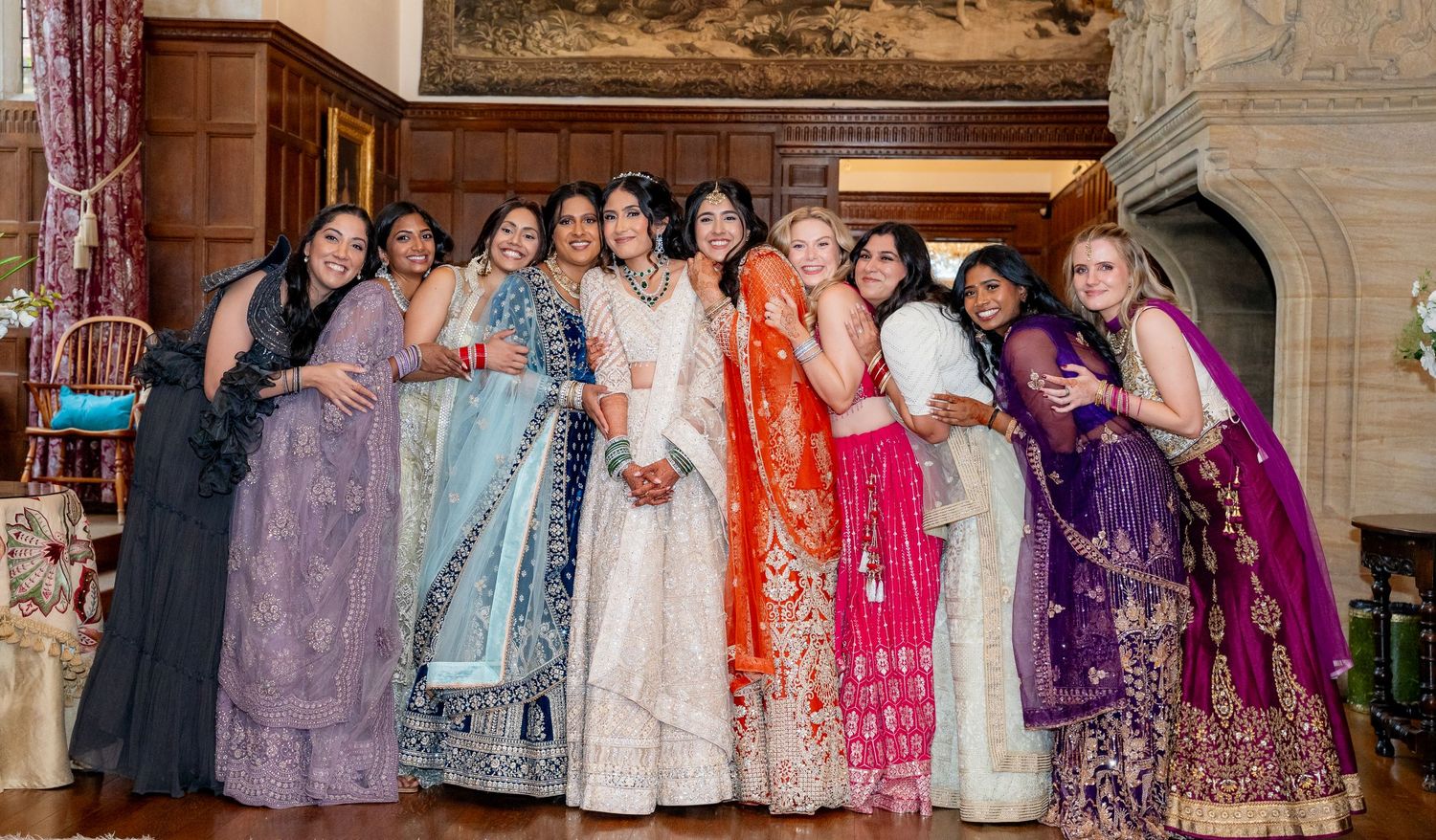 Indian bride in white lehenga posing with bridesmaids in colorful traditional attire.