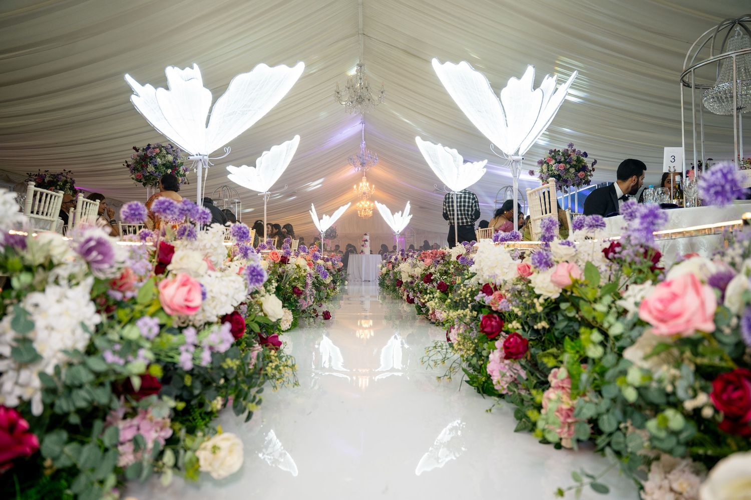 Elegant wedding ceremony aisle decorated with pink and white floral arrangements and white dove decorations under a draped tent.