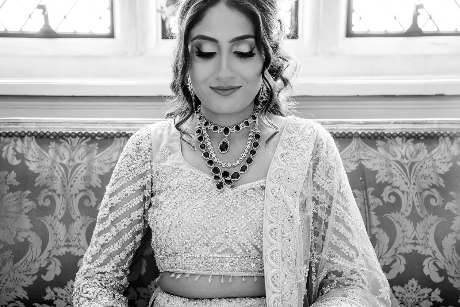 Black and white portrait of bride in embroidered lehenga wearing an elegant dark gemstone necklace.