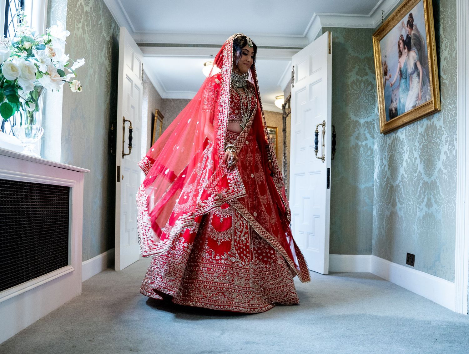 Indian bride twirling in stunning red embroidered lehenga in elegant hallway.