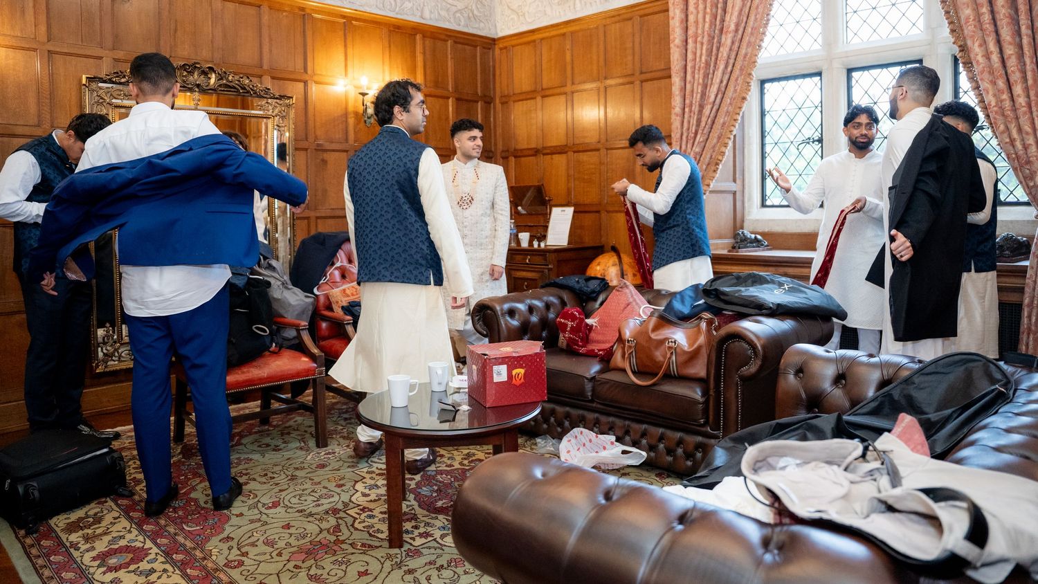Groomsmen in traditional Indian attire getting ready in a wood-paneled room before wedding.