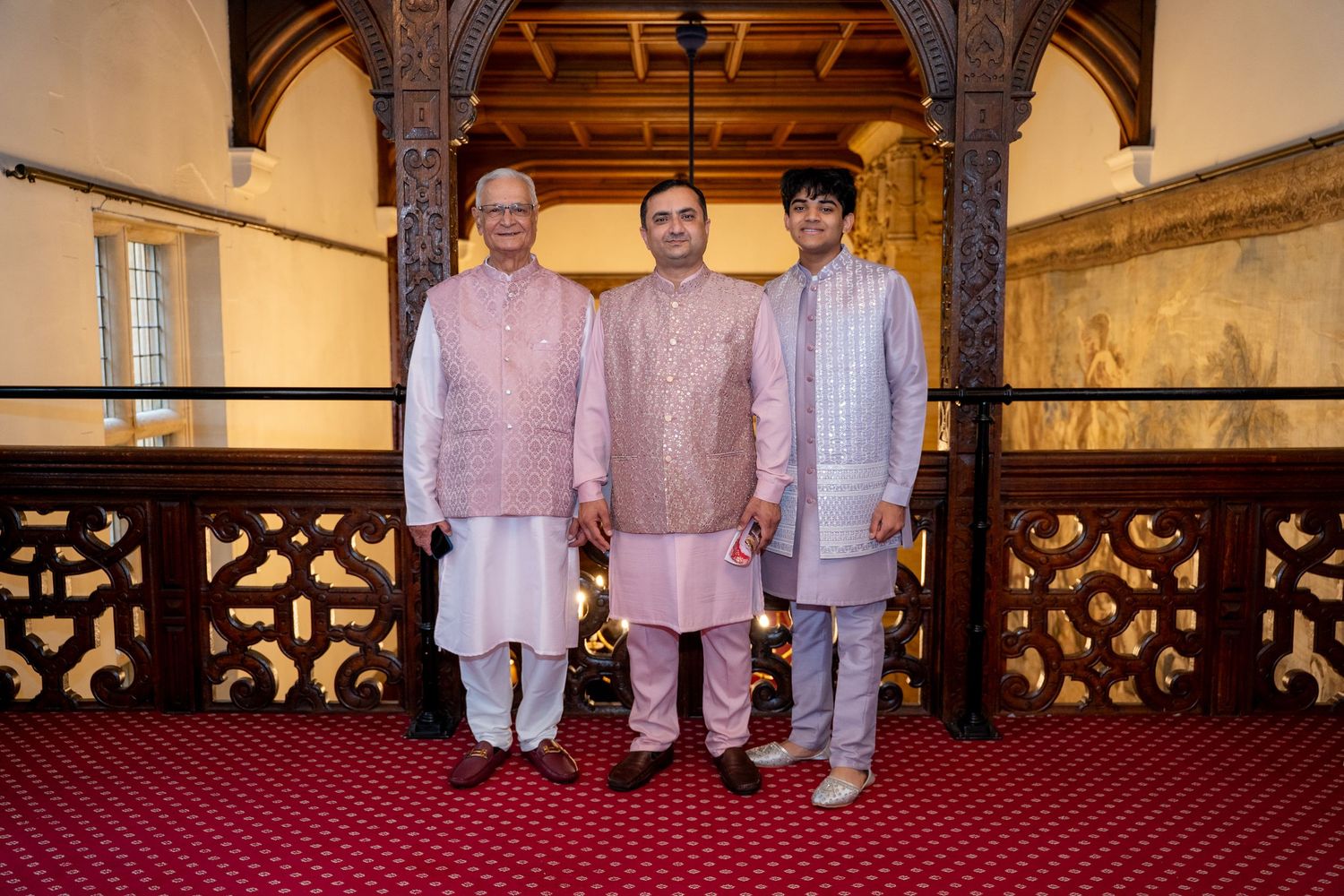 Three Indian men in matching pink kurta pajamas posing together on ornate wooden balcony.