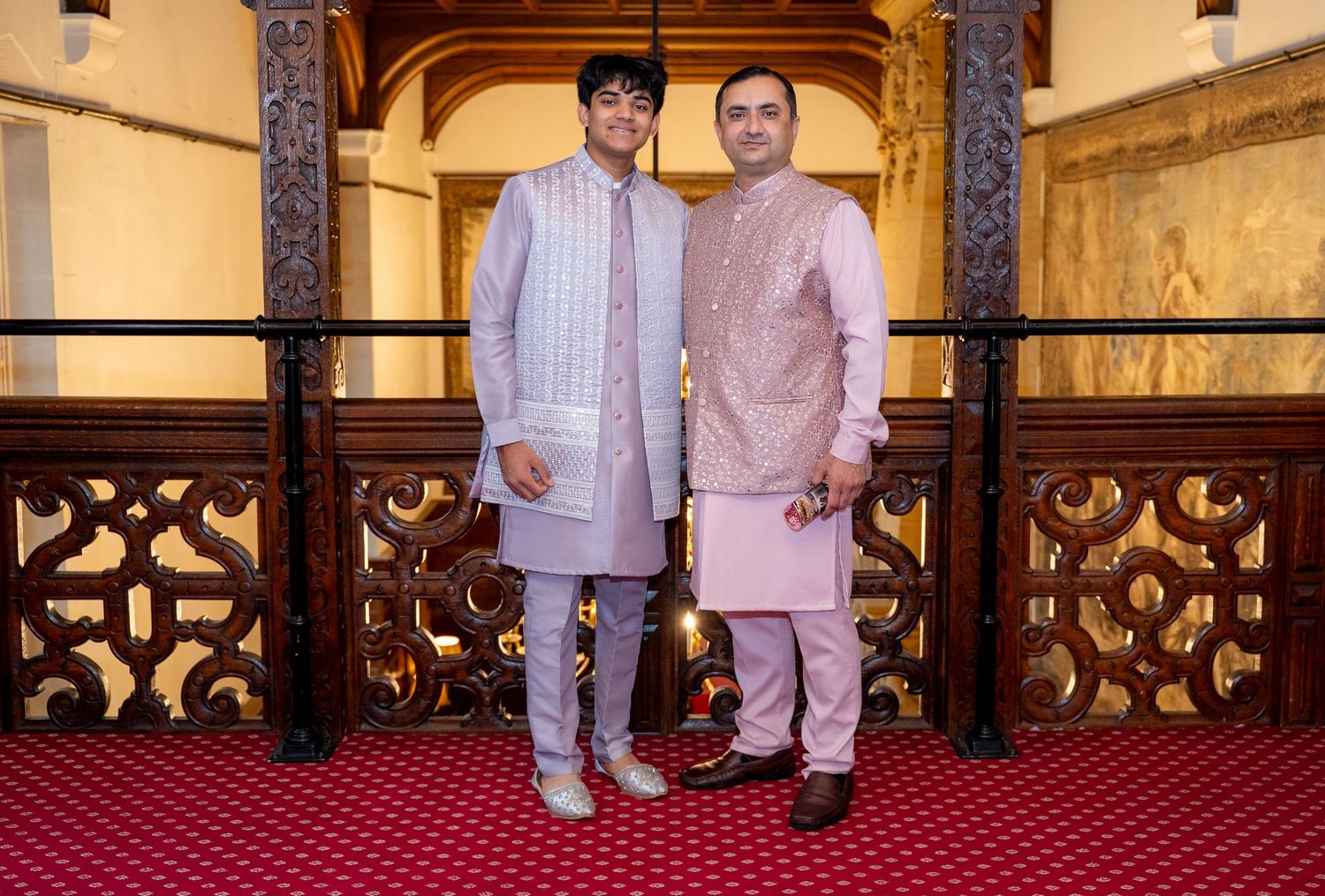 Two men in traditional Indian kurta attire pose together on a balcony with ornate railings.