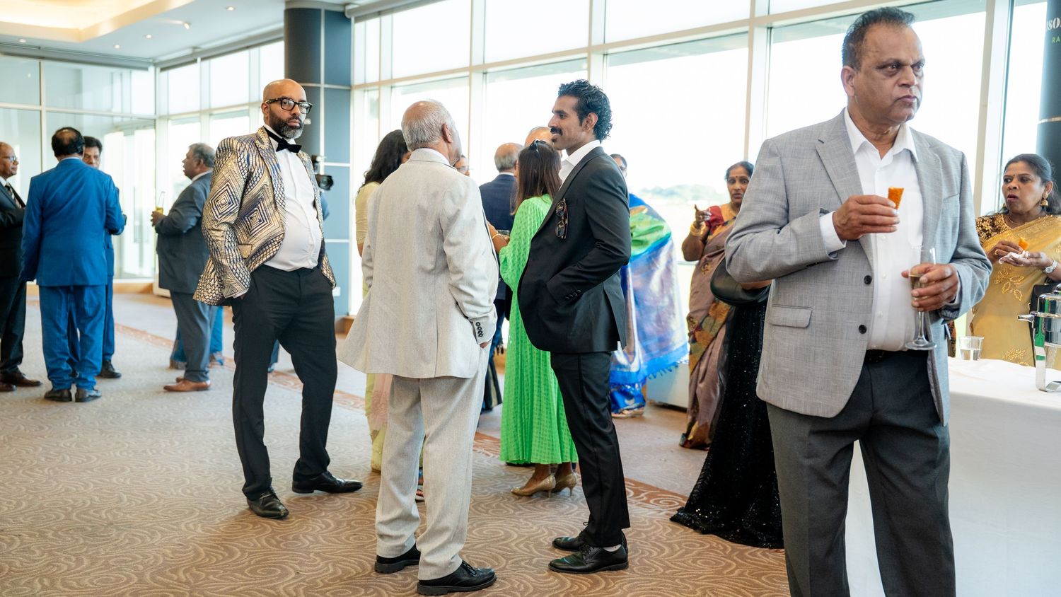 Diverse group of elegantly dressed guests mingling at a formal indoor reception event.