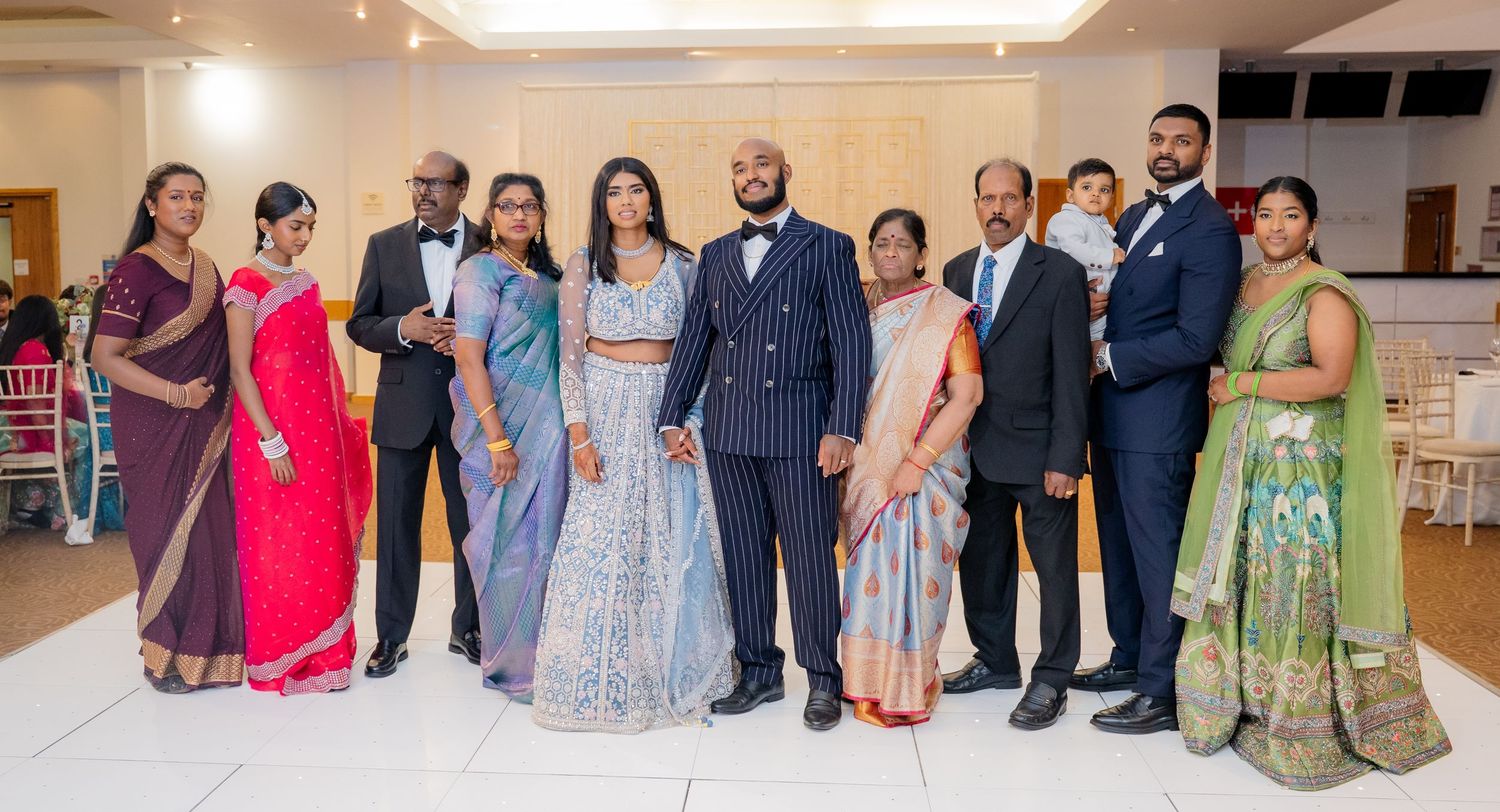 Large wedding family group photo with guests in traditional Indian attire at a reception.