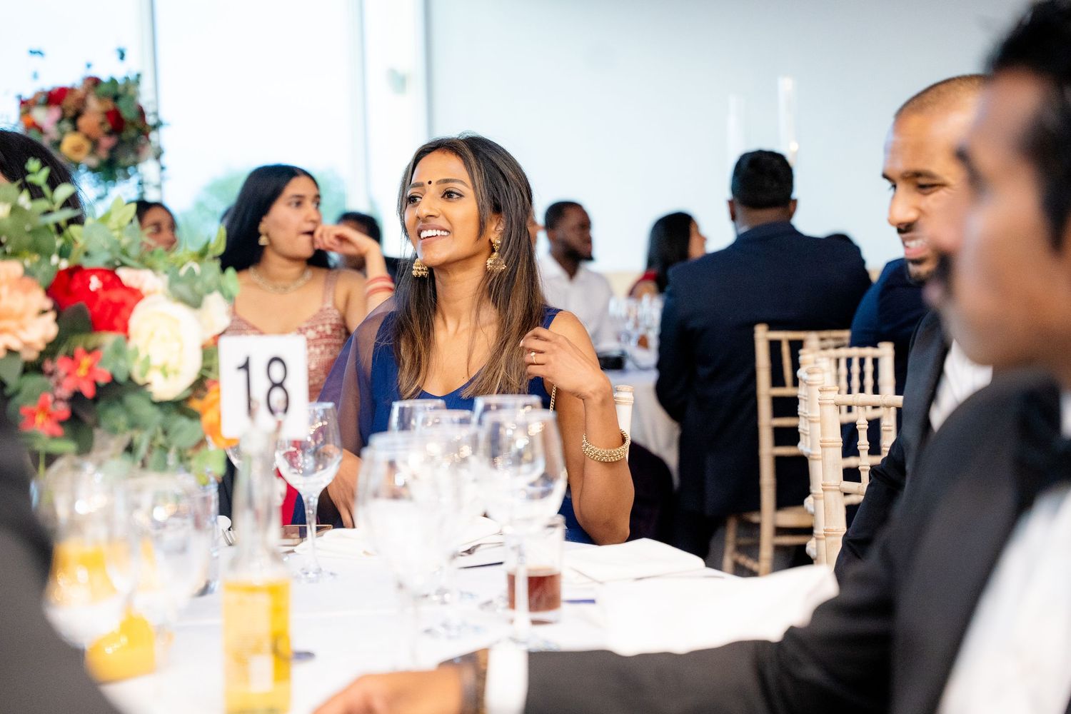 Smiling woman in blue dress enjoying a wedding reception at table number 18.