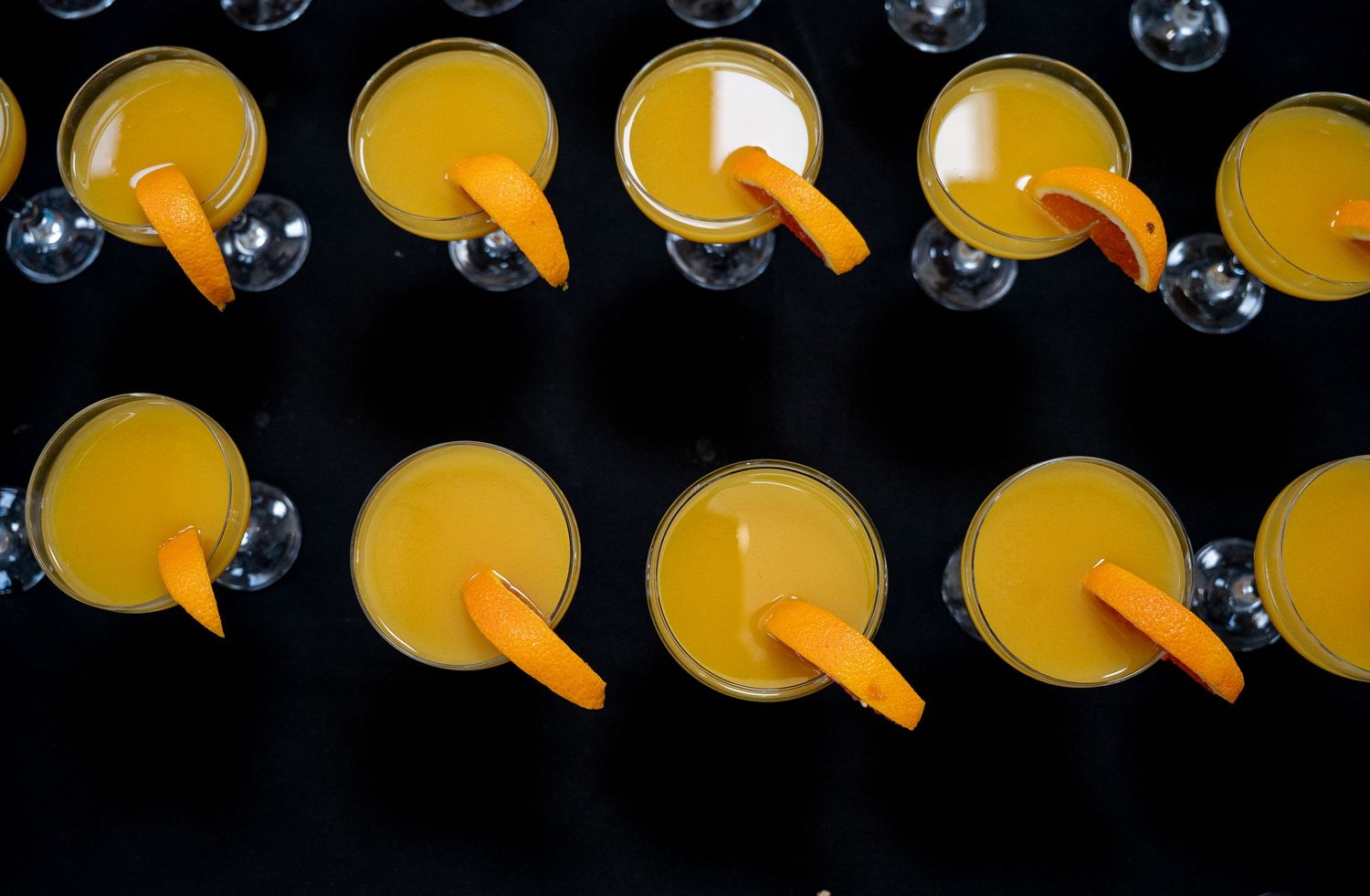 Overhead view of rows of orange juice cocktails garnished with orange slices on a dark surface.