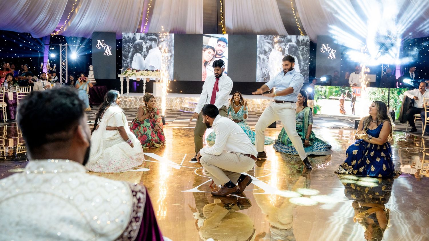 Guests gather on a decorated dance floor during a vibrant Indian wedding celebration inside an elegant tent venue.