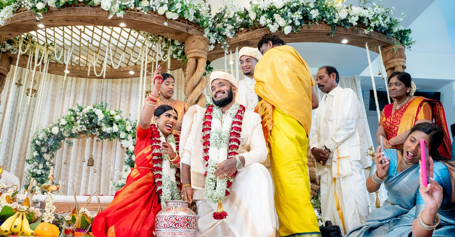 Couple stands under ornate mandap during colorful Hindu wedding ceremony surrounded by family.