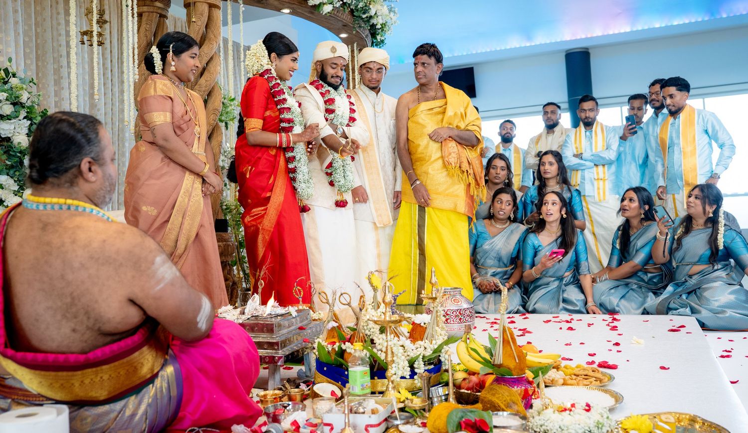 Traditional South Indian wedding ceremony with bride in red saree and groom in white at decorated mandap.