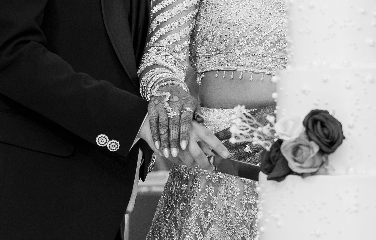 Black and white close-up of bride with henna hands and groom holding a gift box at wedding.