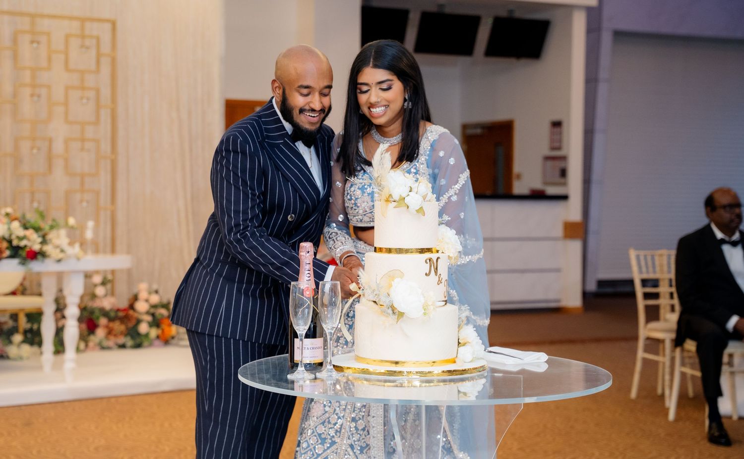 Groom in pinstripe suit and bride cut elegant tiered wedding cake at reception.