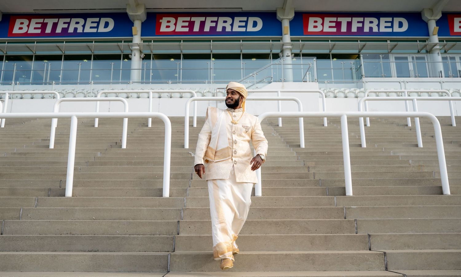 Man dressed in elegant white traditional outfit descending steps at a Betfred-sponsored stadium.