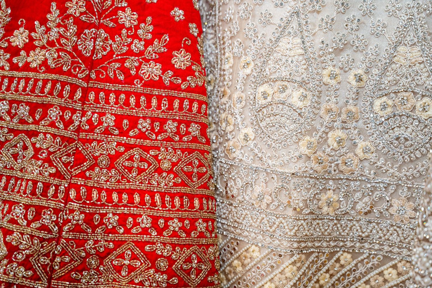 Close-up of intricate gold embroidery on red Indian bridal lehenga fabric beside white dupatta.