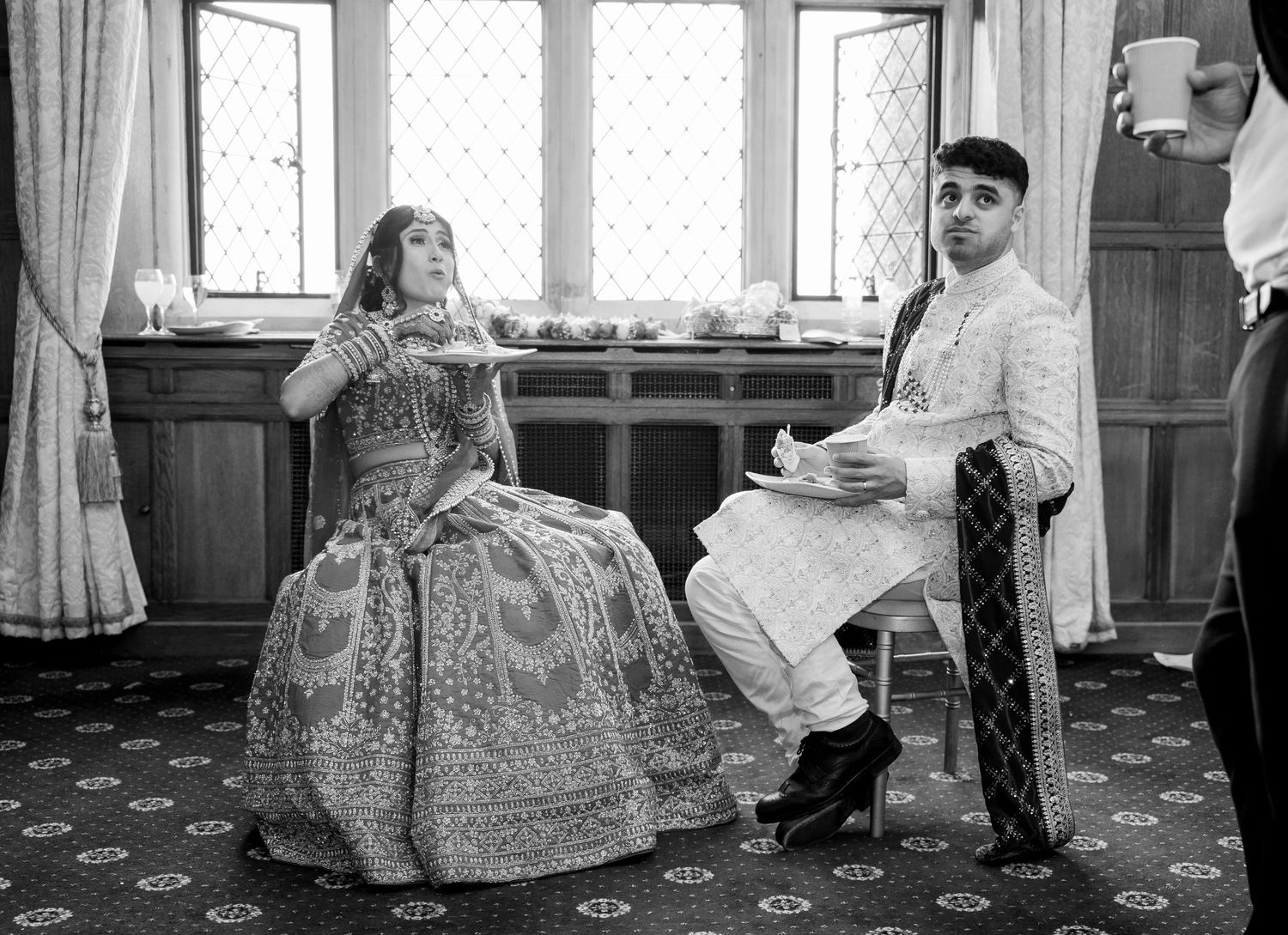 South Asian bride and groom in traditional attire sit together in black and white wedding photo.