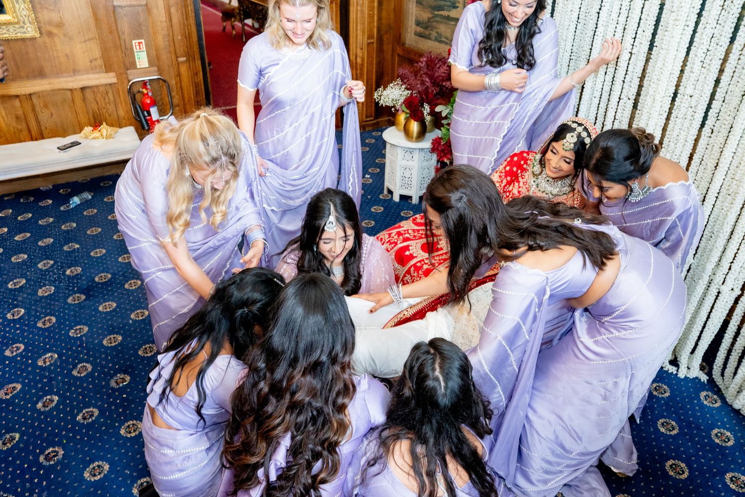 Bridesmaids in lavender saris surround a bride in a joyful wedding celebration huddle.