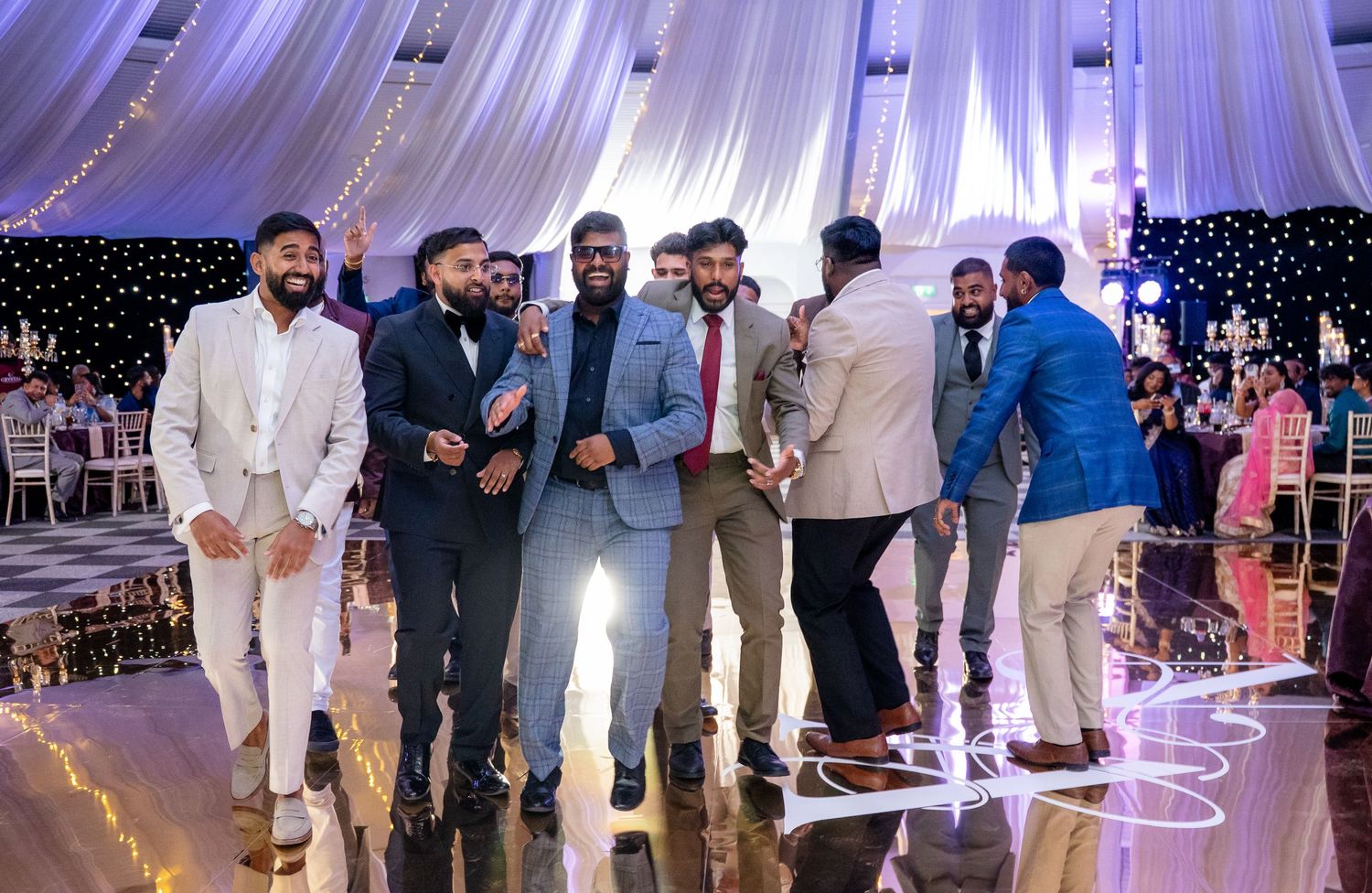 Joyful group of men in formal suits celebrating and laughing together at a wedding reception.