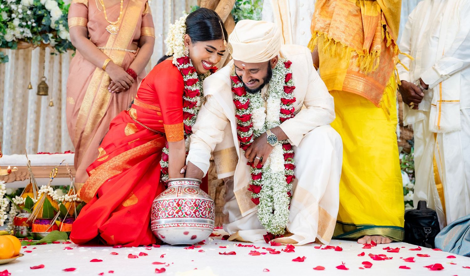 Indian bride and groom performing traditional Hindu wedding ceremony with rose petals and decorative pot.