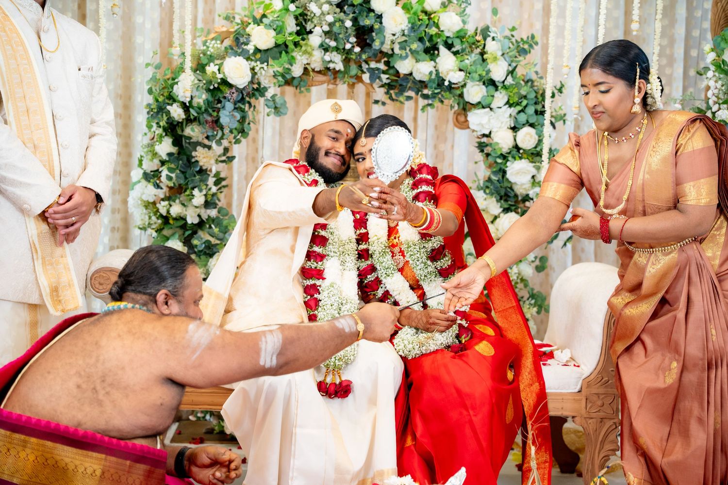 Priest performs rituals as bride and groom exchange garlands at colorful South Indian wedding ceremony.