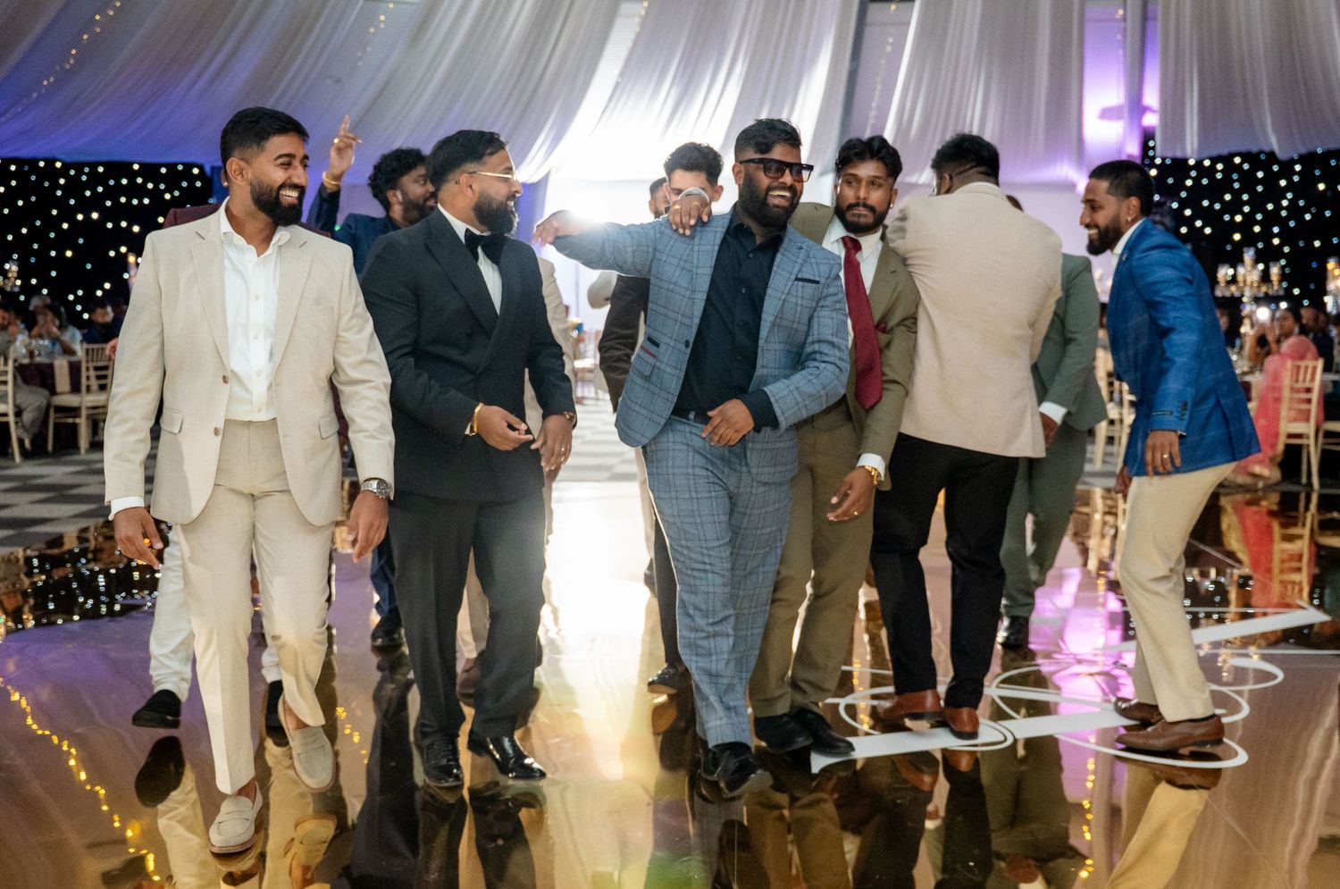 Group of well-dressed groomsmen celebrating and dancing together on the dance floor at a wedding reception.