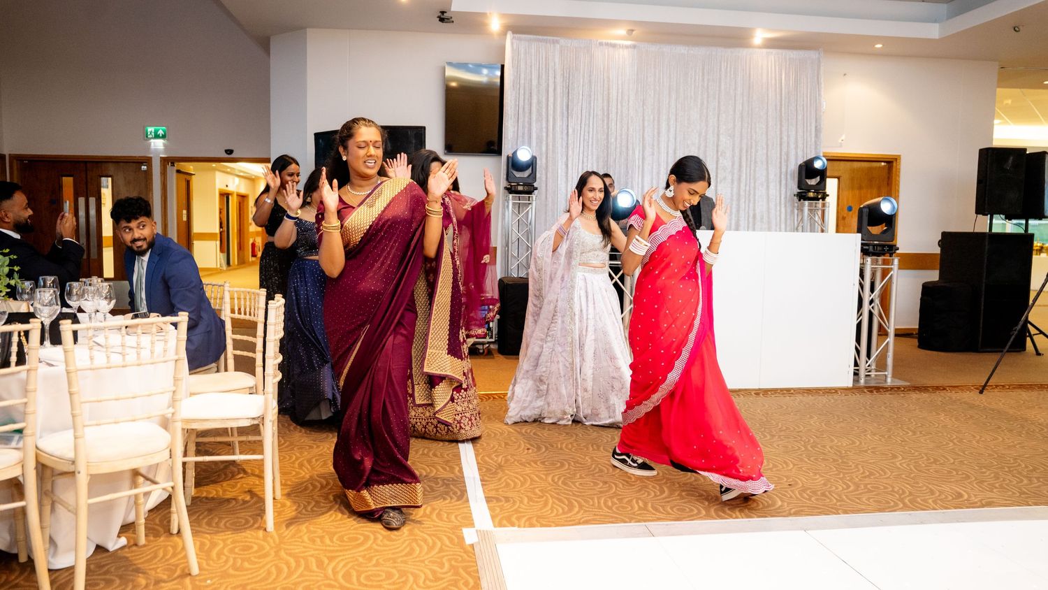 Women in vibrant sarees dancing at an Indian wedding reception celebration.