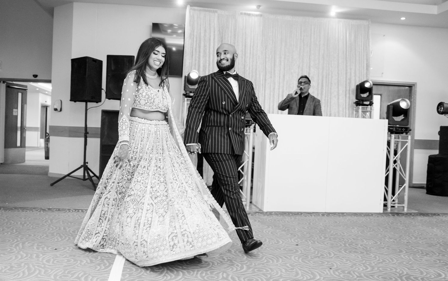 Black and white photo of bride in flowy lehenga and groom in pinstripe suit dancing at wedding.