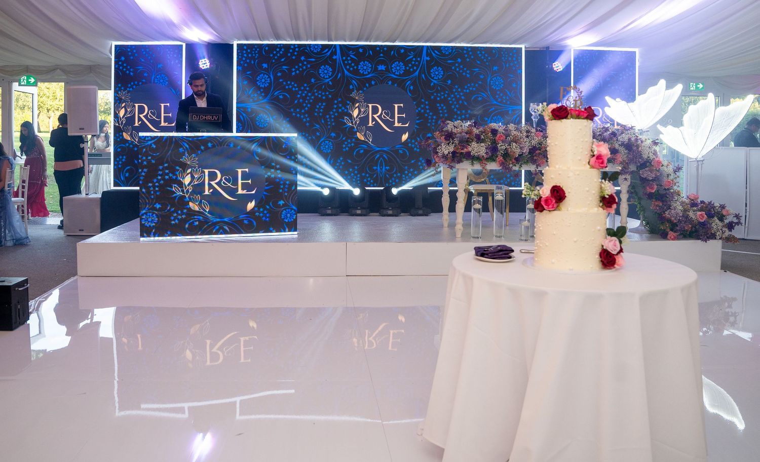 Elegant wedding reception venue with illuminated R&E monogram backdrop and decorated three-tier white cake.