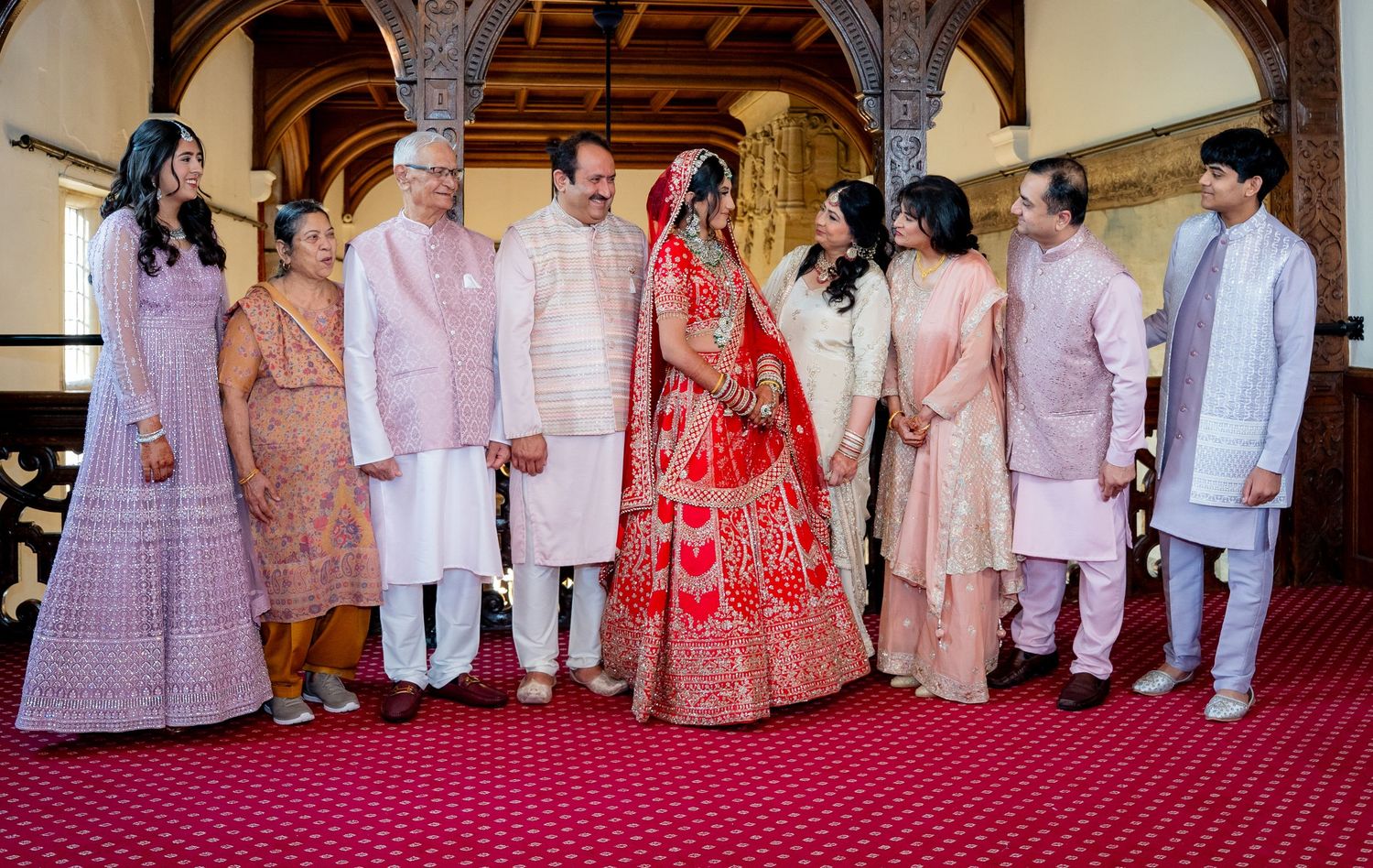 Indian bride in red bridal lehenga poses with family members in traditional attire.