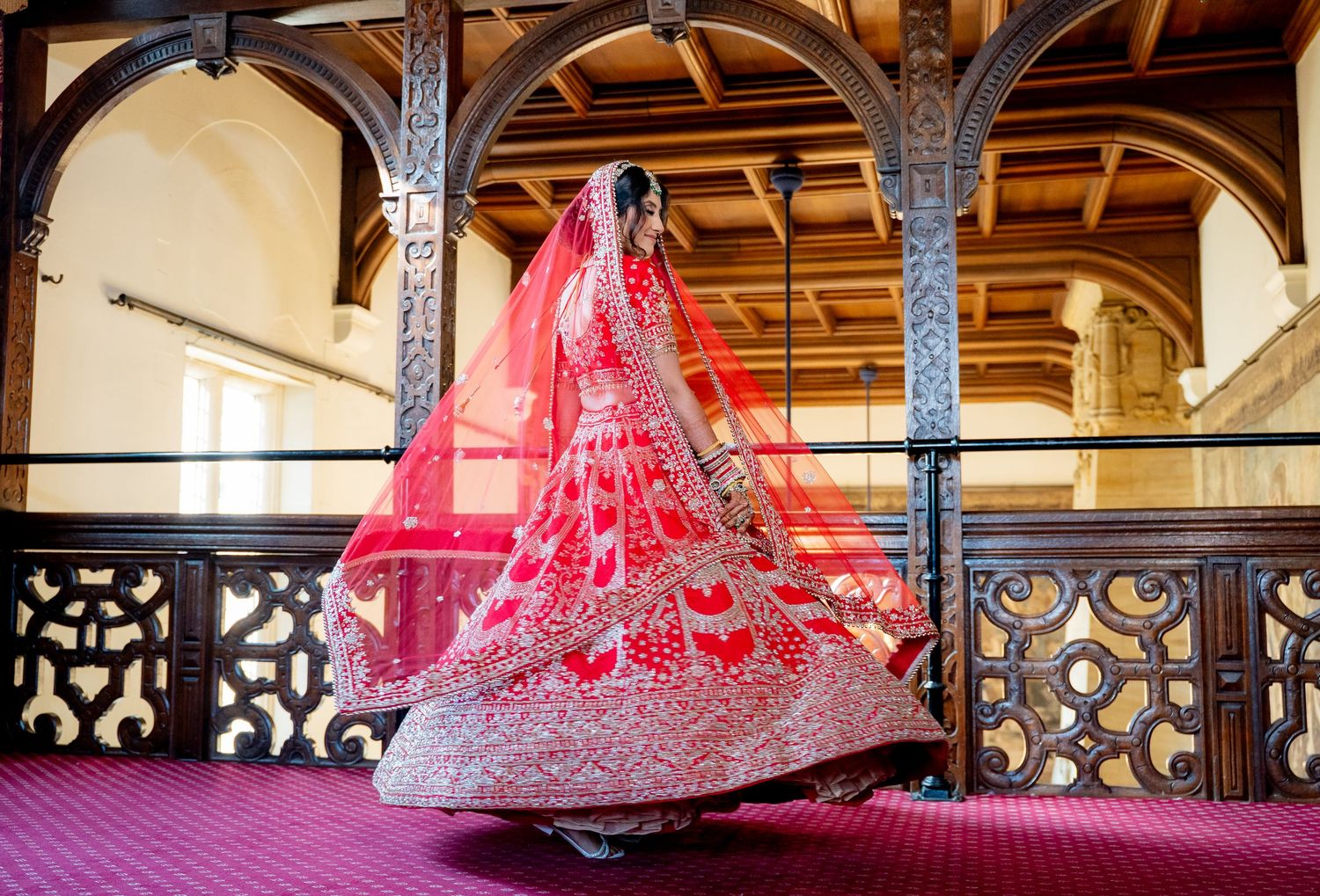 Indian bride in stunning red embroidered lehenga twirls in a grand historic venue.