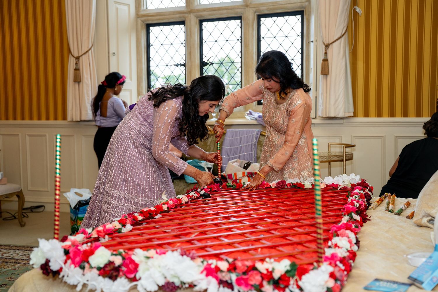 Women preparing a traditional red and white floral wedding decoration on a large table indoors.
