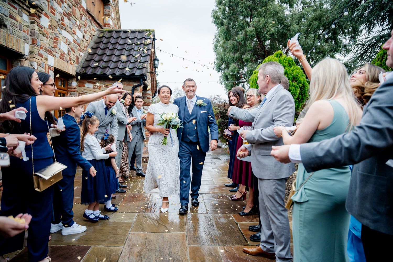 Bride and groom walking through confetti shower surrounded by cheering guests at rustic venue.