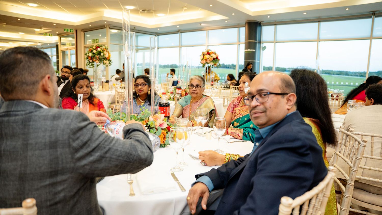 Guests in formal wear enjoy conversation and drinks at an elegantly decorated wedding reception.