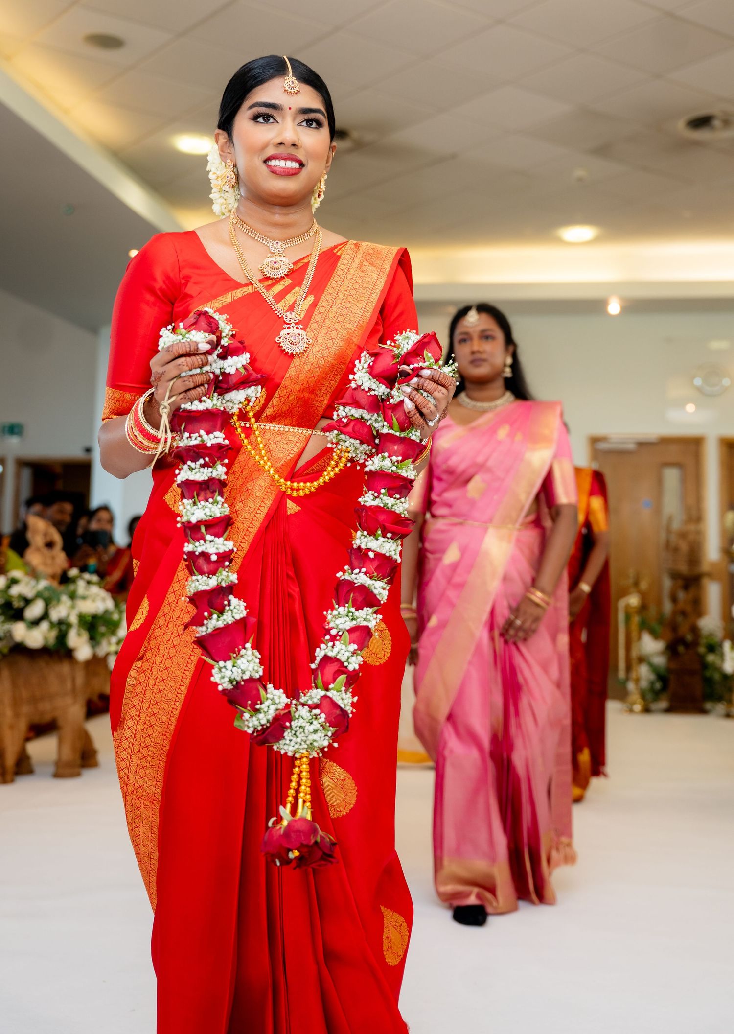 Close-up of South Indian bride in red saree holding floral garlands at traditional wedding.
