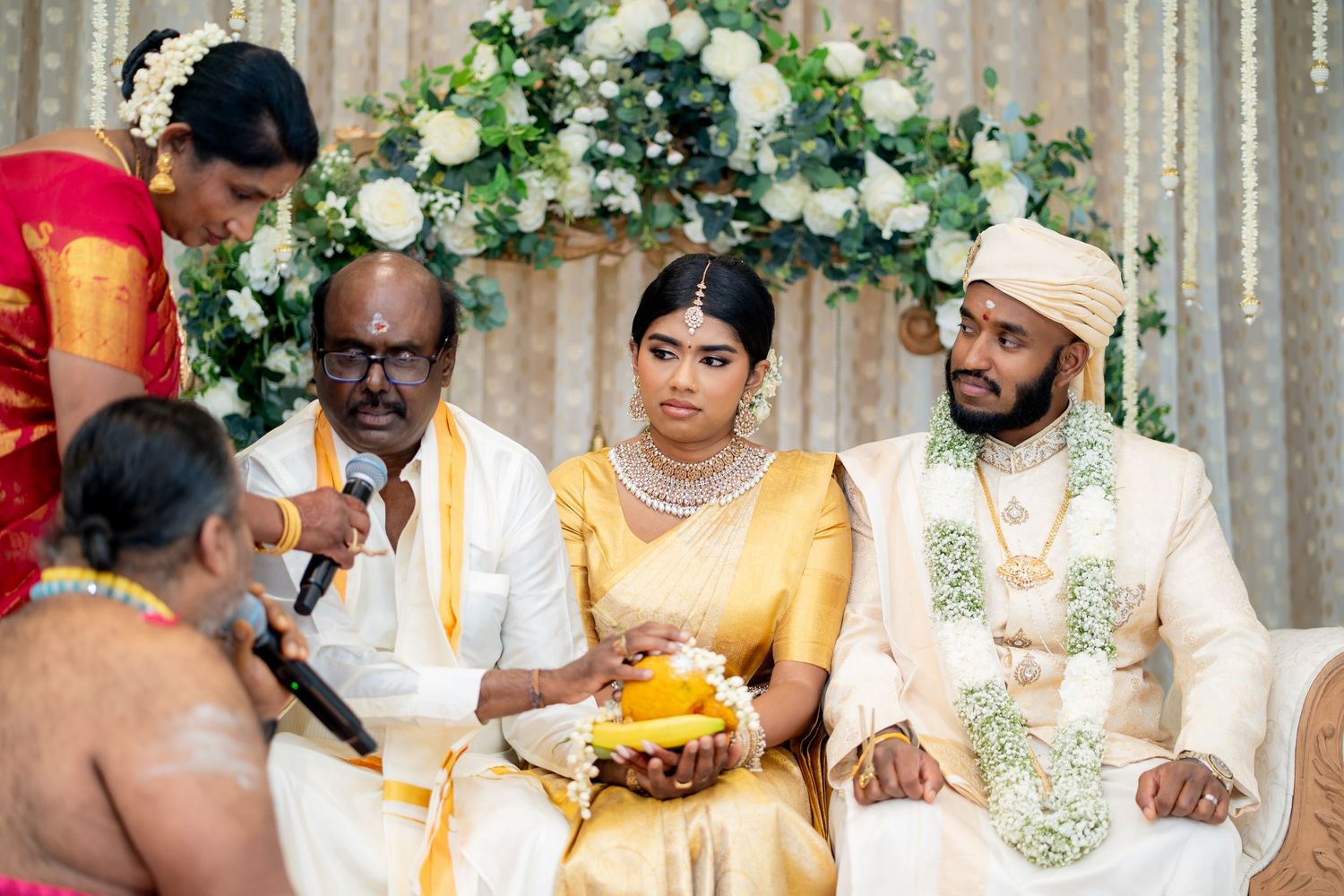 Hindu wedding ceremony with bride in gold silk saree and groom in white attire during sacred rituals.