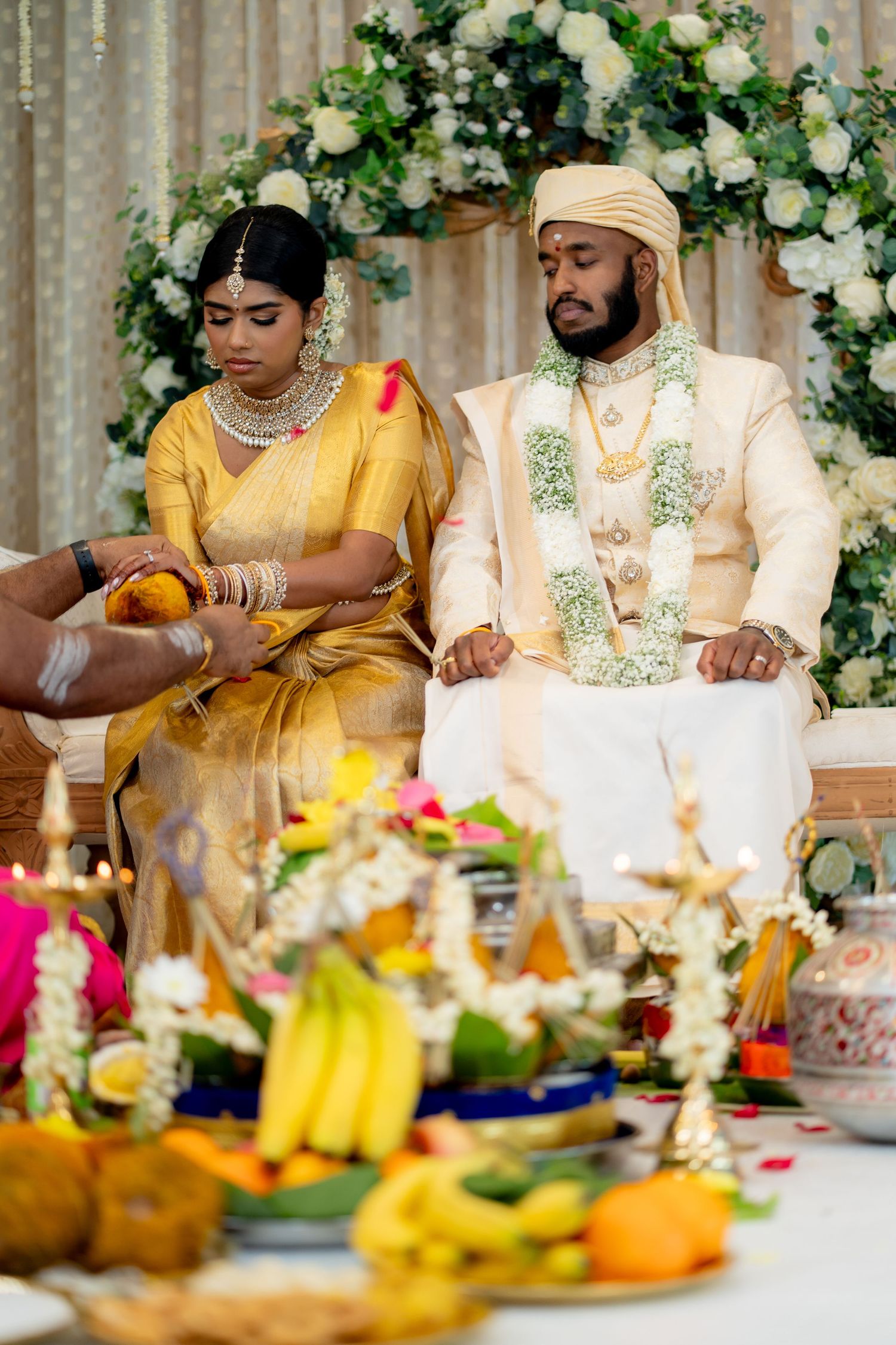 Hindu wedding couple in traditional attire performing sacred rituals before decorated altar with flowers and offerings.