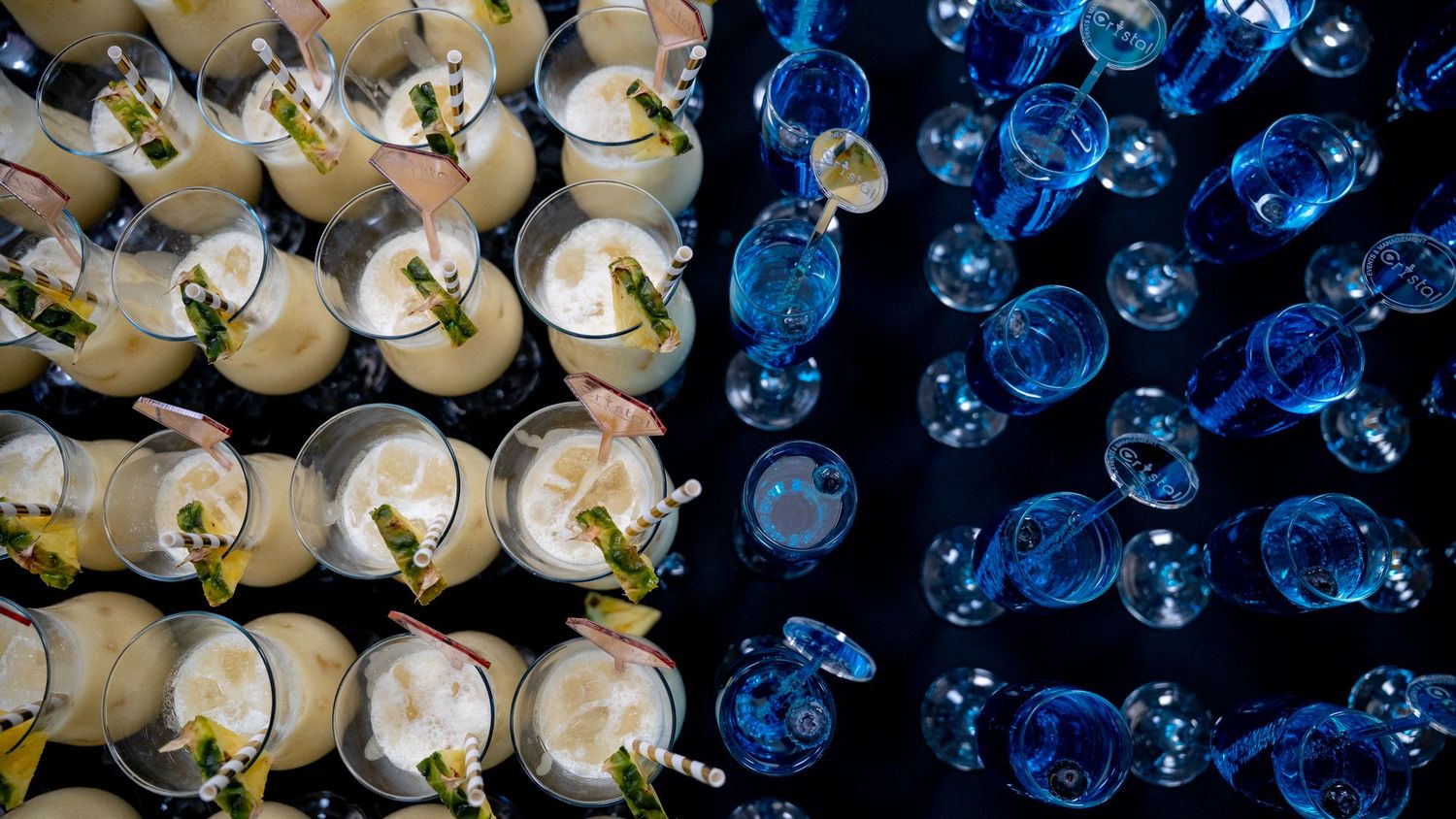 Aerial view of yellow and clear cocktails arranged in rows under blue lighting.