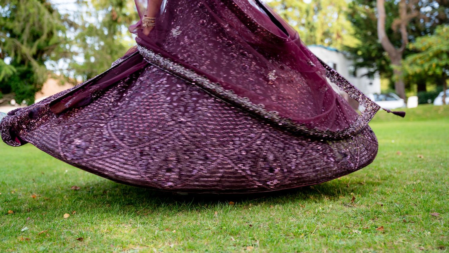 Close-up of a purple embroidered lehenga skirt twirling gracefully on a green grass lawn at a wedding.